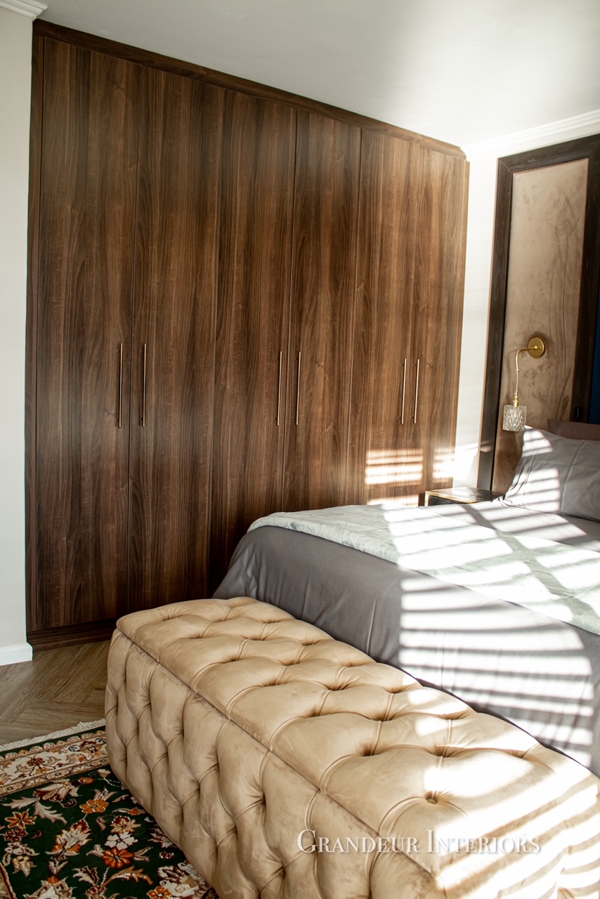 Walnut built-in wardrobes with brass handles and tufted ottoman