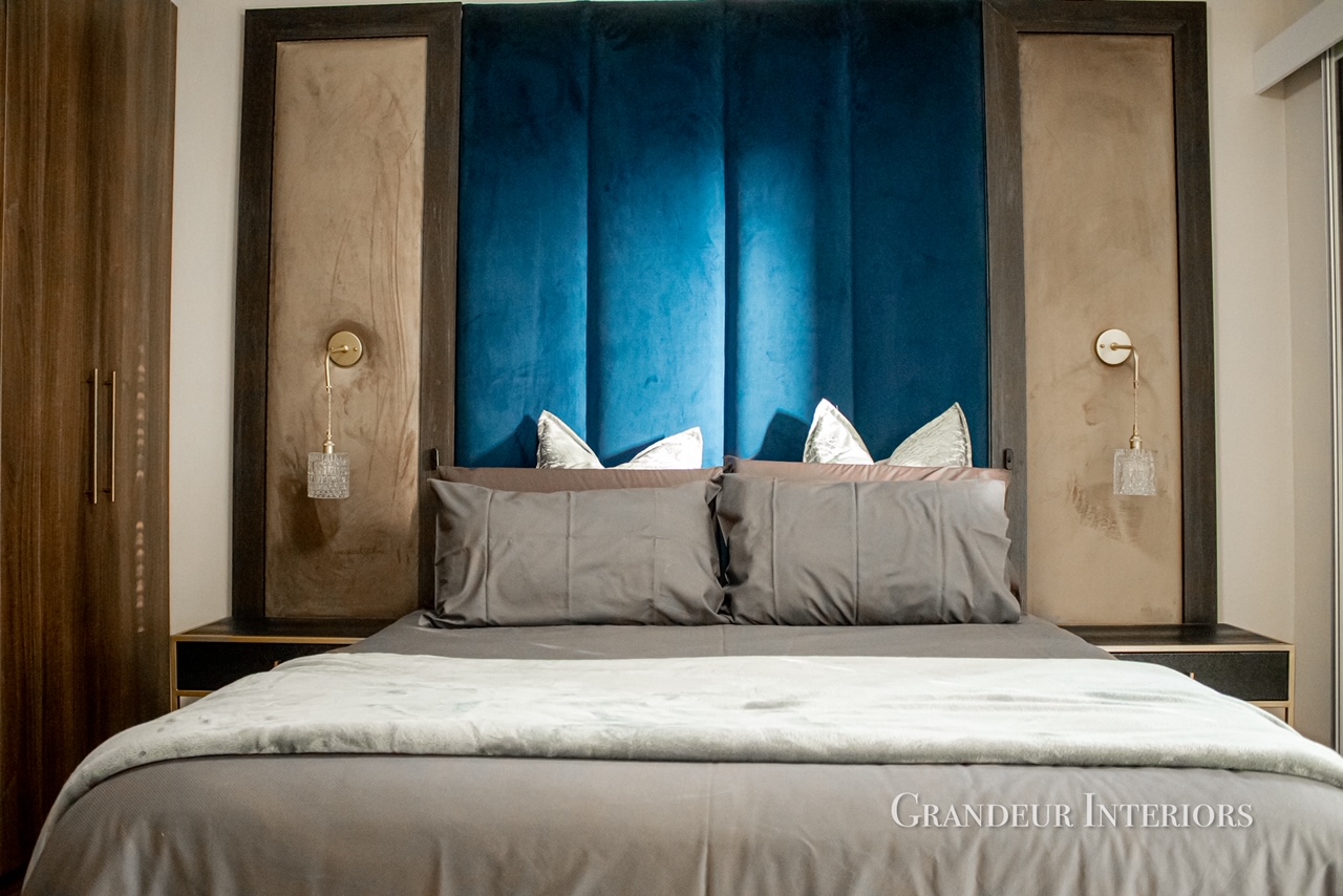 Master bed with deep blue velvet panelled headboard, timber frames and brass sconces