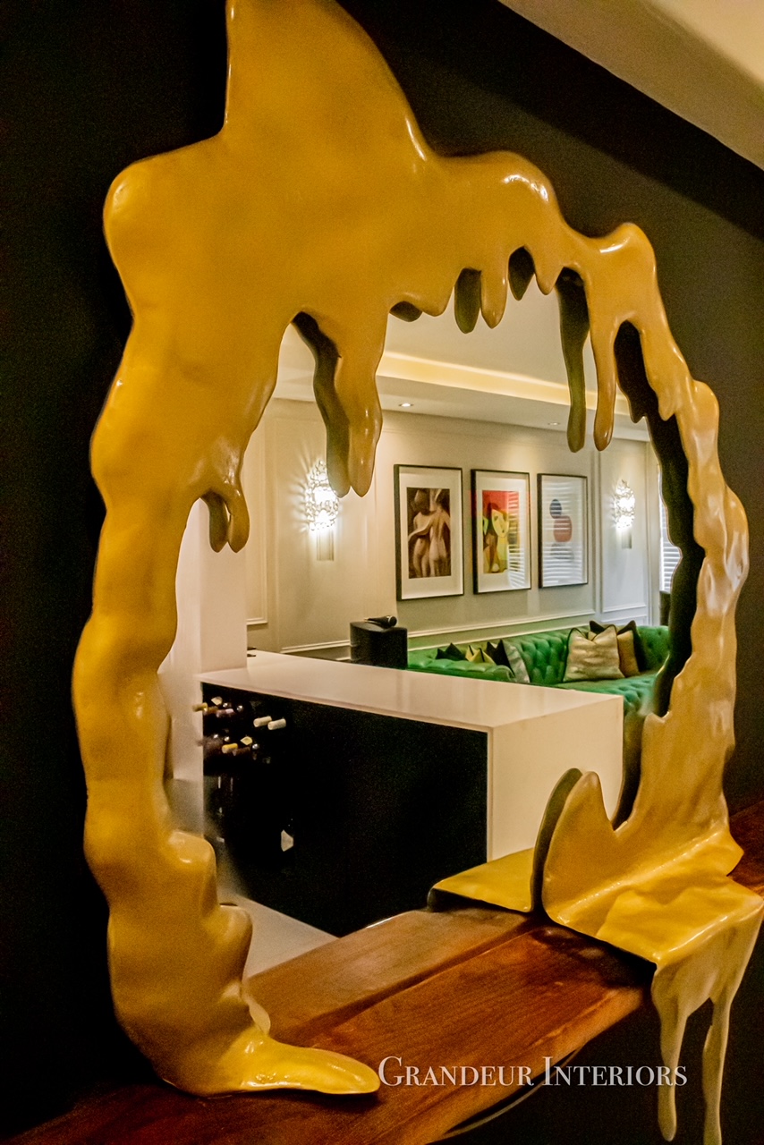 Sculptural gold drip mirror above timber console in the bar area
